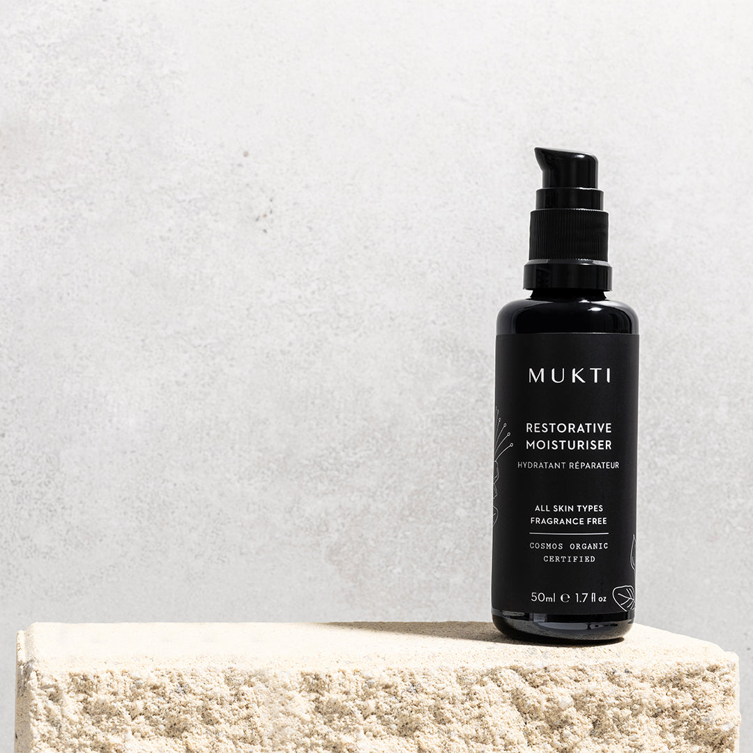 Mukti Organics | Restorative Moisturiser | Lifestyle Image - black pump bottle displayed on a stone block against a light gray background