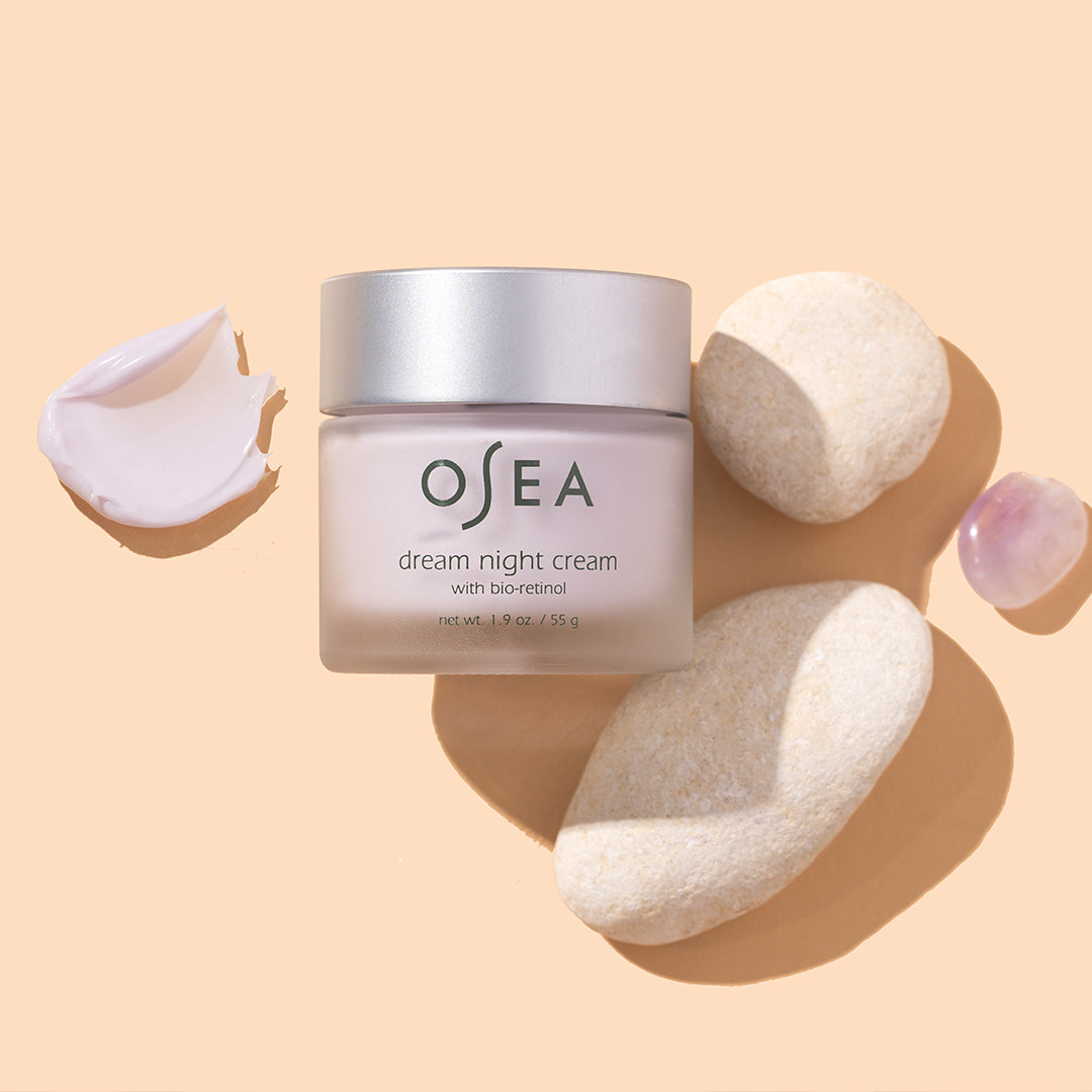OSEA | Dream Night Cream | Styled Image with Swatch - jar styled with cream swatch, smooth stones, and pink crystal on a beige background