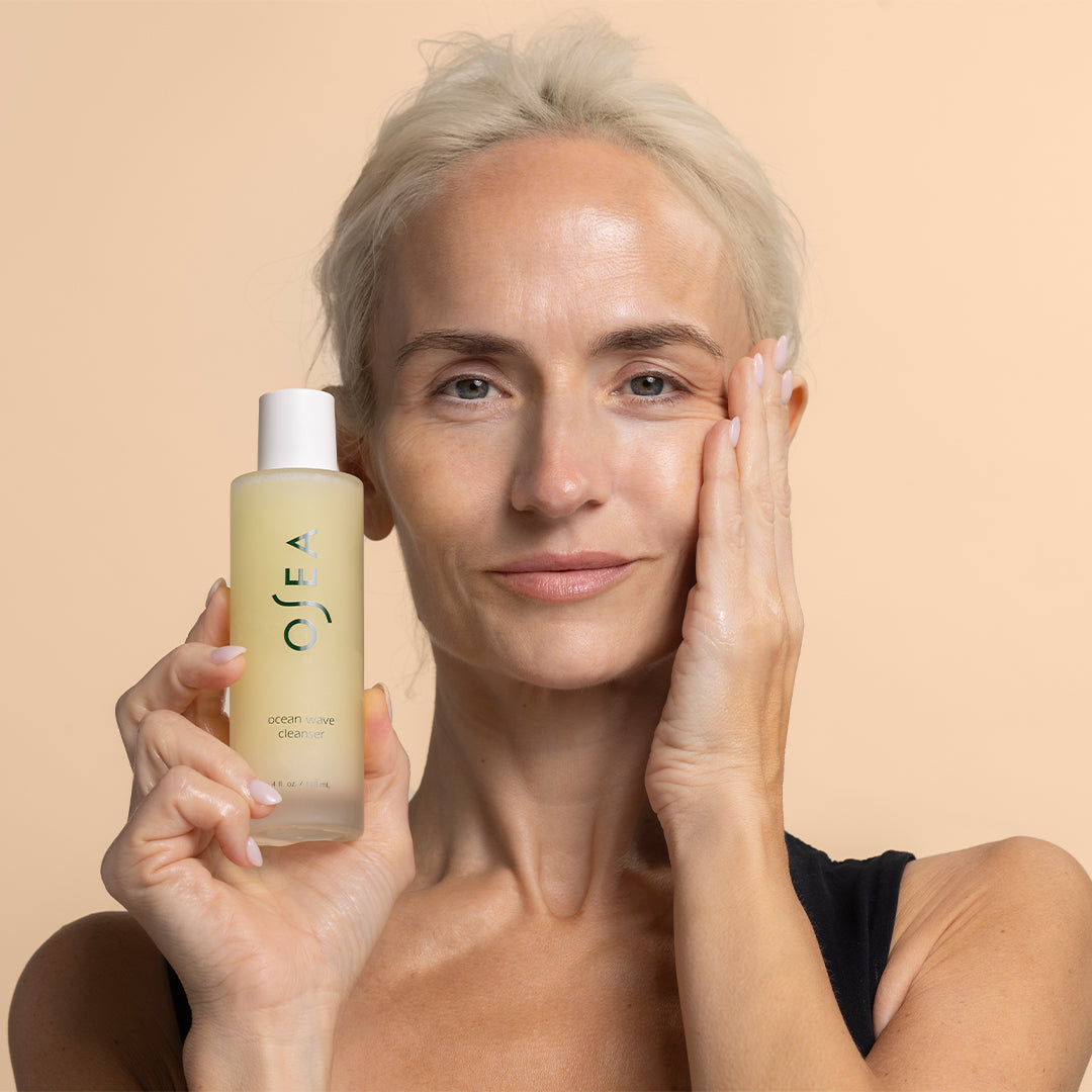 OSEA | Ocean Wave Cleanser | Model Image_Sep26 - person cleanser bottle against a peach background