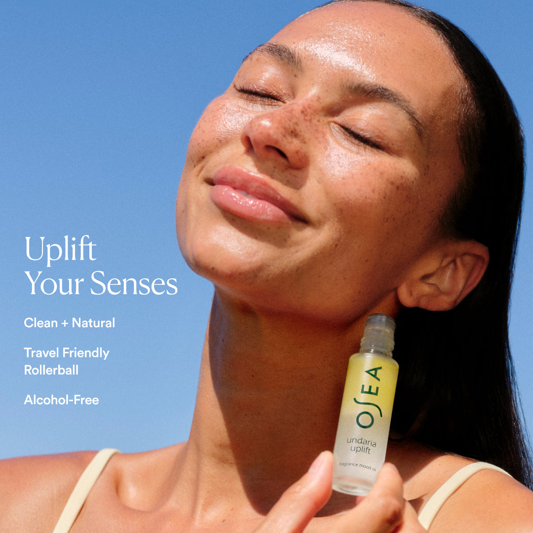 OSEA | Undaria Uplift Fragrance Mood Oil | Model Lifestyle Image - model holding rollerball against her neck with blue sky background