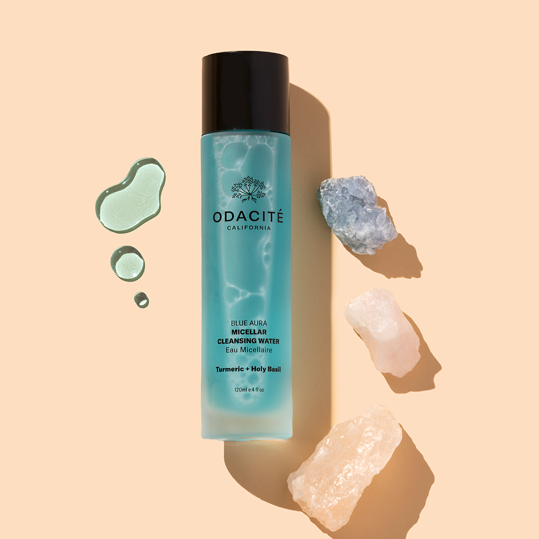 Odacité | Blue Aura Micellar Cleansing Water | Product Image with Swatch -  bottle with blue liquid swatches and crystals on a beige background