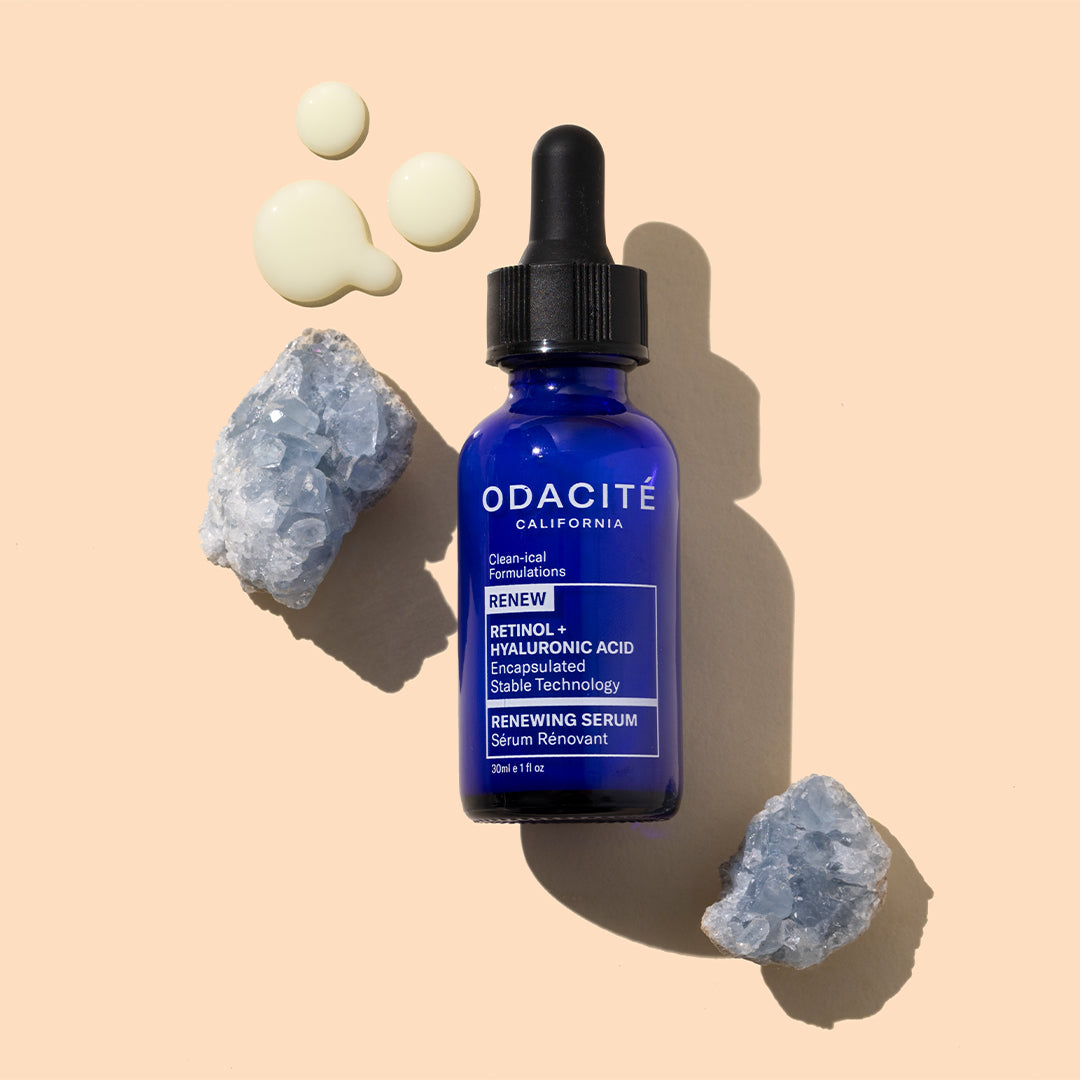 Odacite | Retinol & Hyaluronic Acid Serum | Styled Image with Swatch_Sep26 - blue dropper bottle with serum swatches and crystals on a peach background