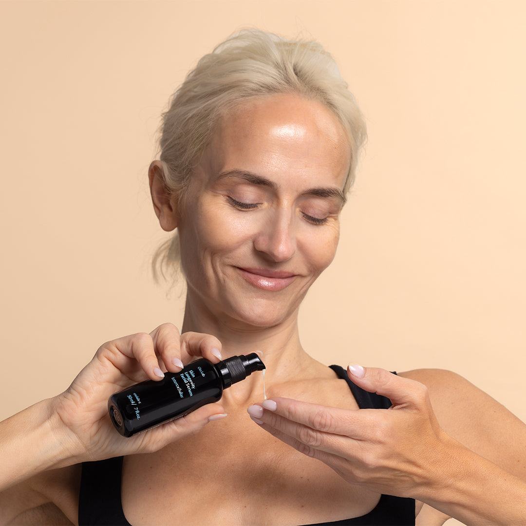 Oio Lab | Intercellular Skin Longevity Serum | Model Image_Sep26 - model dispensing serum from a black bottle applied to skin against a peach background