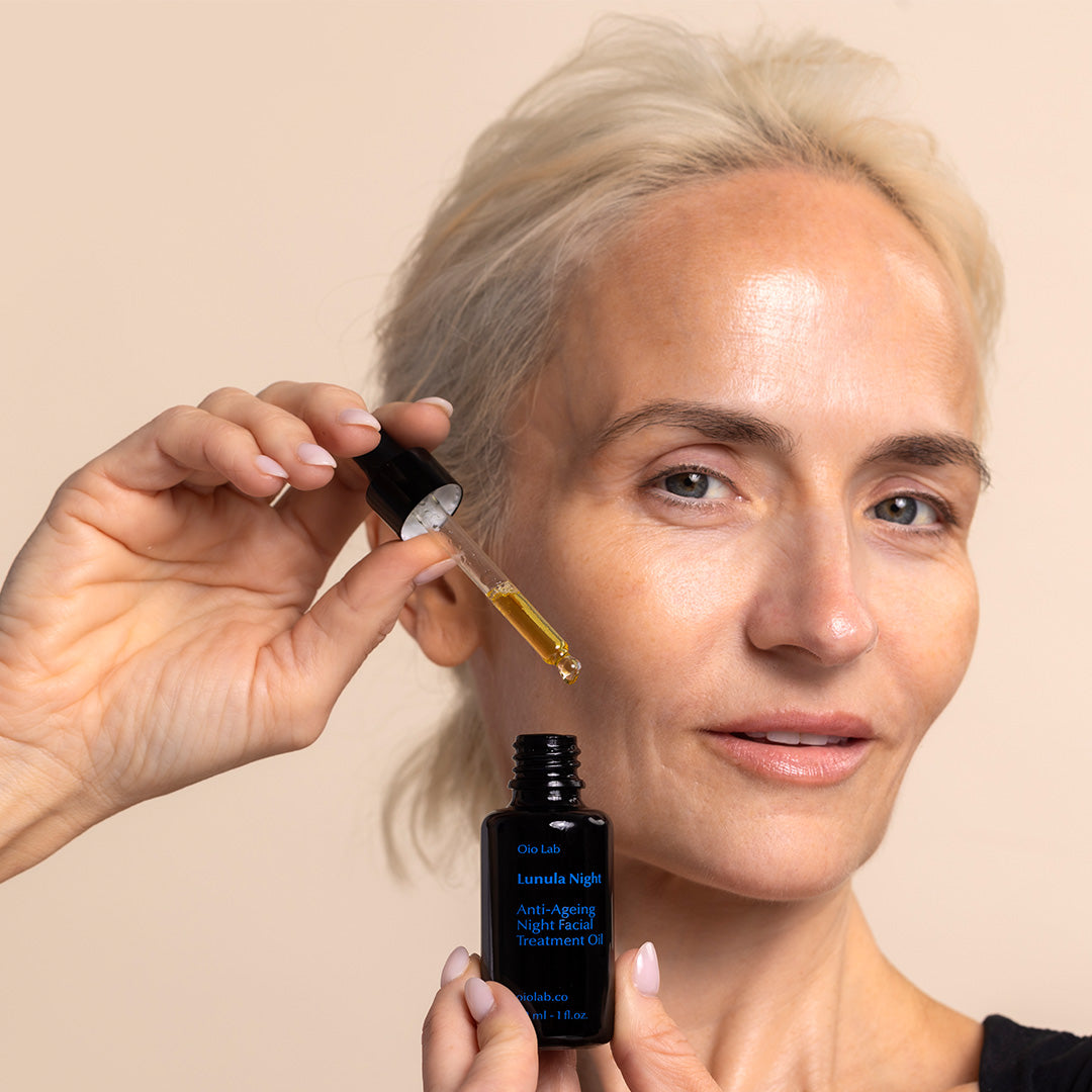 Oio Lab | Lunula Night Anti-Aging Night Facial Treatment Oil | Model Image, model holding dropper bottle near face