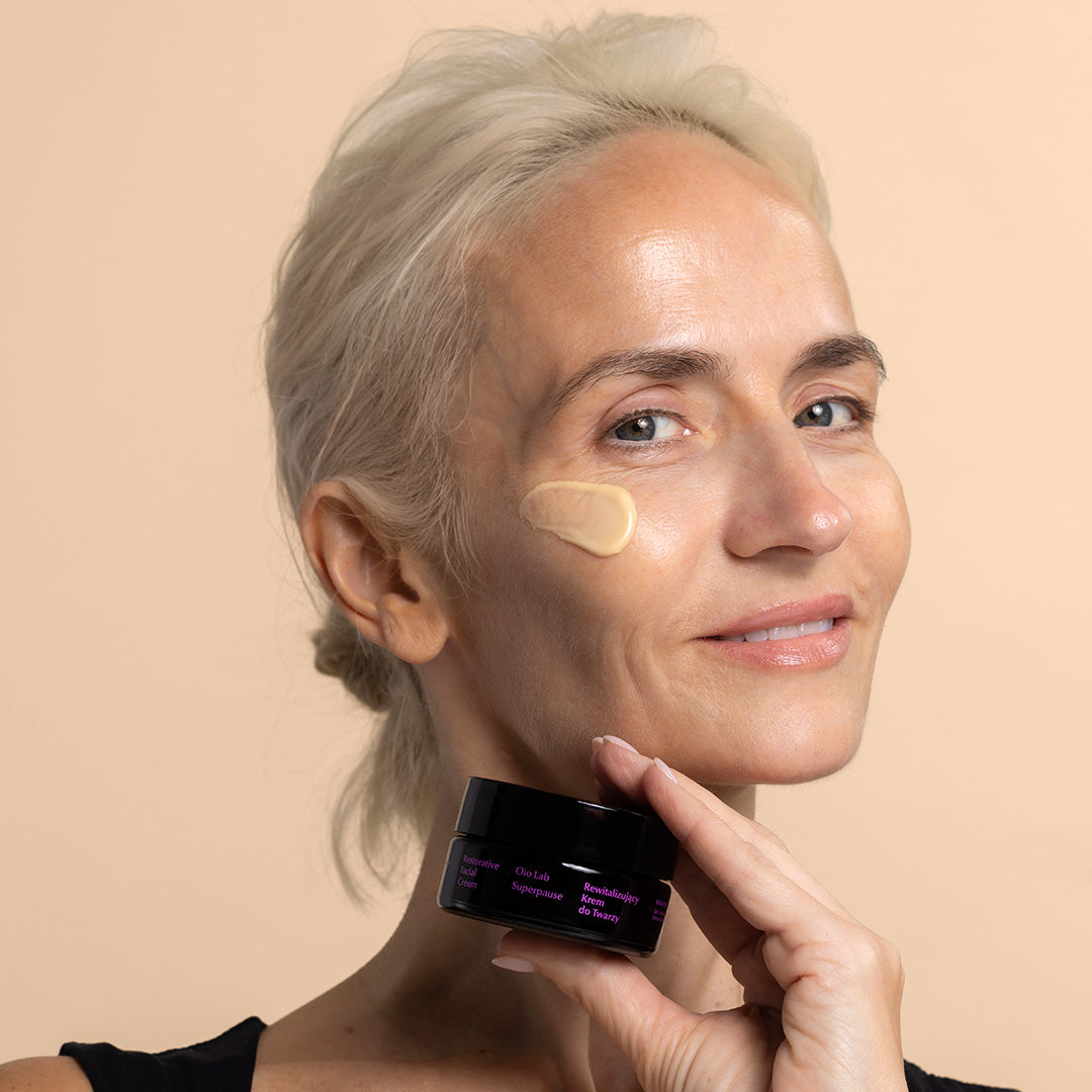 Oio Lab | Superpause Restorative Facial Cream | Model Image, model holding black jar with purple writing, cream swatch applied to face