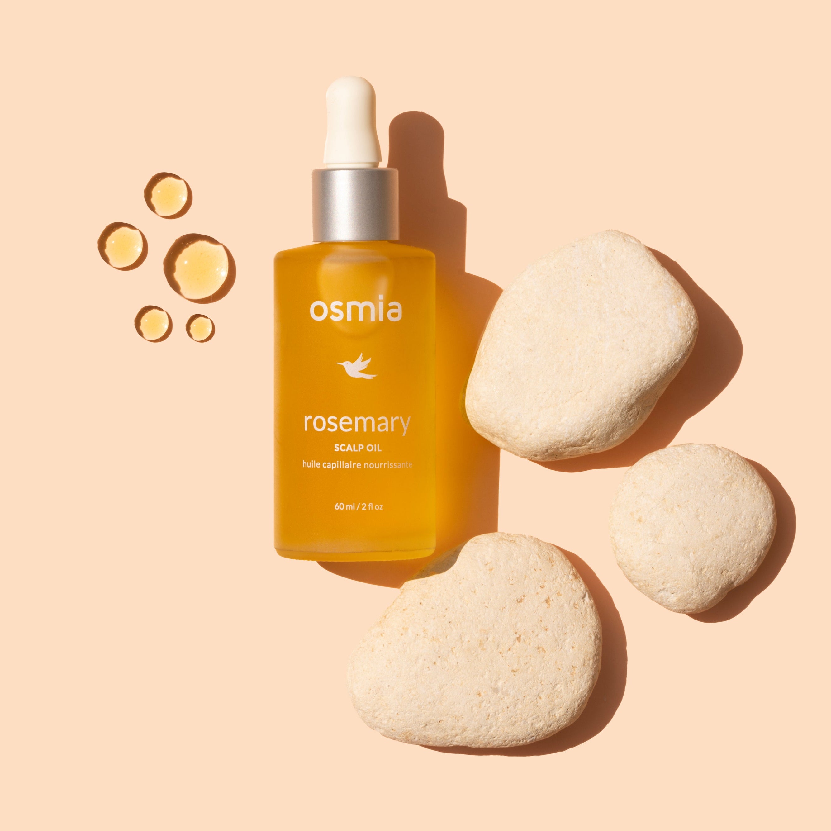 Osmia Rosemary hair oil bottle with stones on a beige background