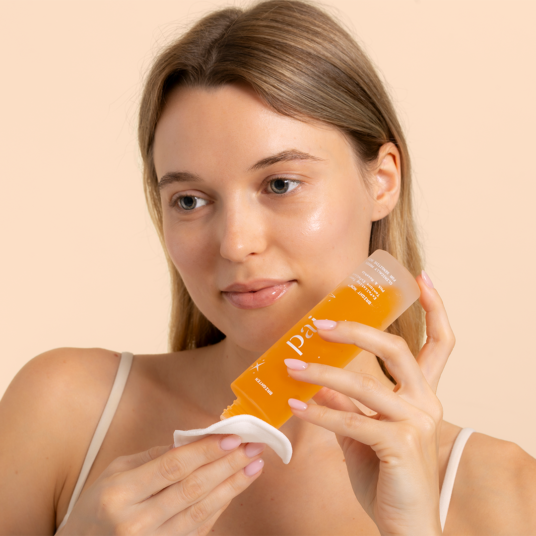 Pai Skincare | Bright Now PHA & Rosehip Exfoliating Toner | Model Image - woman pouring toner onto a cotton pad against a neutral background