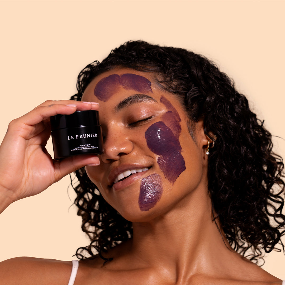 Plumtox | Clarifying Enzyme Mask | Model Image A_Jul26 - model with mask applied to the face while holding jar beside one eye