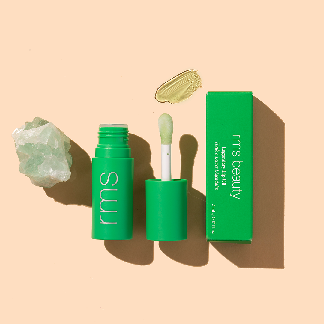 RMS Beauty | Chameleon Lip Oil | Product Image - lip Oil with applicator, green packaging, swatch, and crystal on a beige background