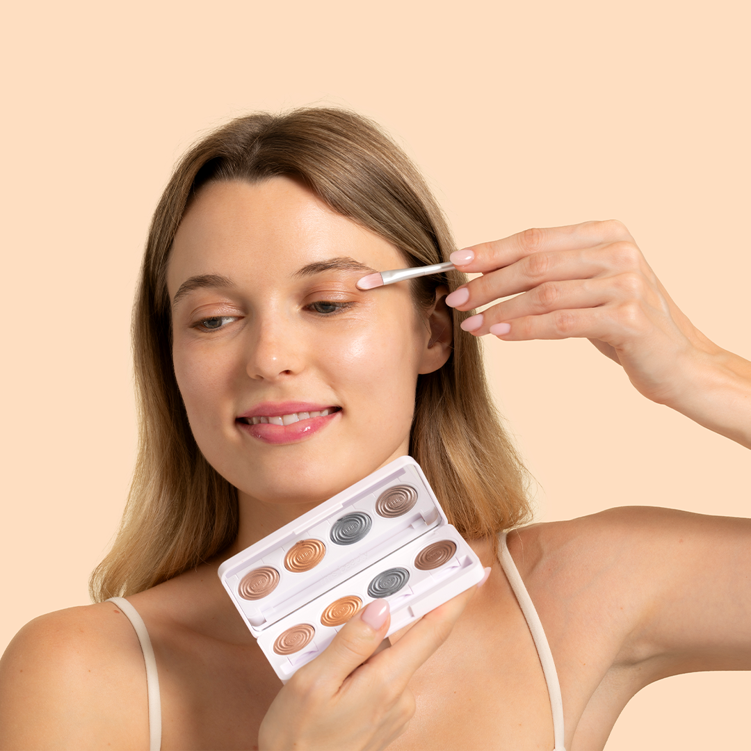 RMS Beauty | ReDimension Hydra Eyes Quartet | Model Image - Woman applying eyeshadow with a small brush shown on a beige background