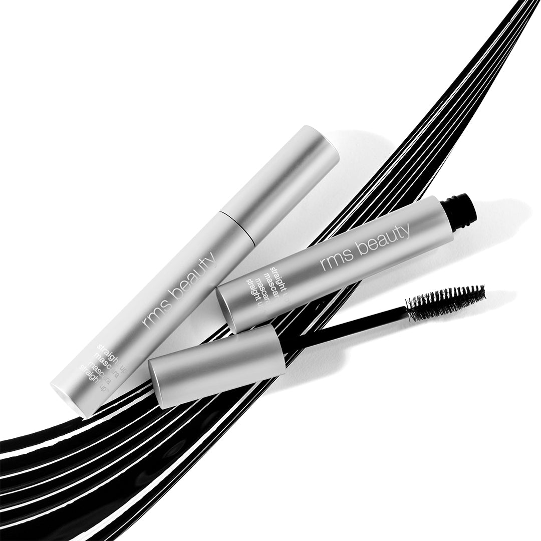 RMS Beauty | Straight Up Volumizing Peptide Mascara | Lifestyle Image - mascara in silver tubes with an open black mascara wand, styled over sweeping black mascara strokes on a white background
