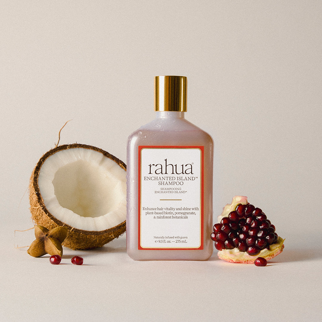 Rahua | Enchanted Island Shampoo | Lifestyle Image - shampoo bottle with a gold cap displayed beside coconut and pomegranate