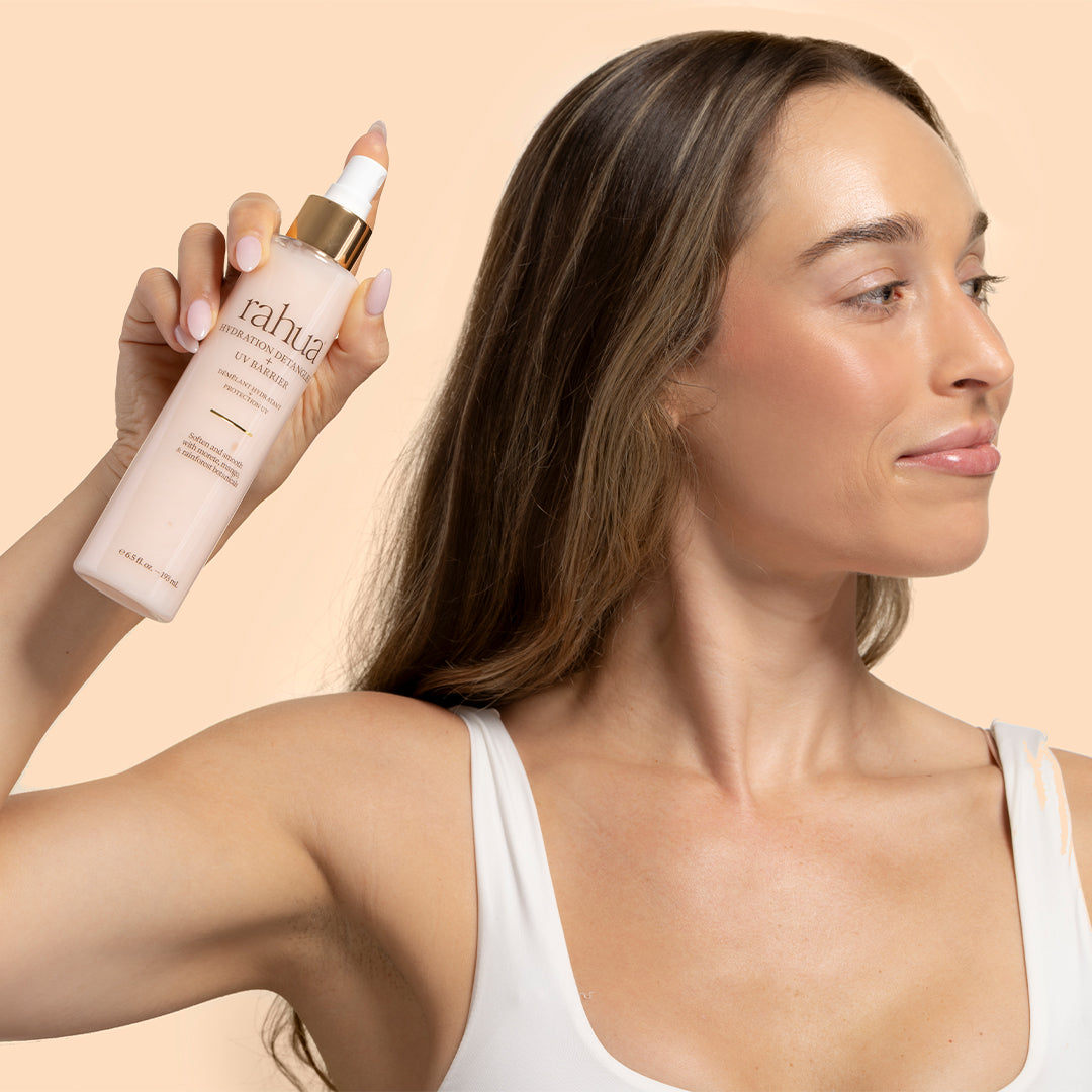 Rahua | Hydration Detangler + UV Barrier | Model Image_Aug26 - model holding a pale pink bottle with a white spray pump and gold collar beside her hair against a light beige background