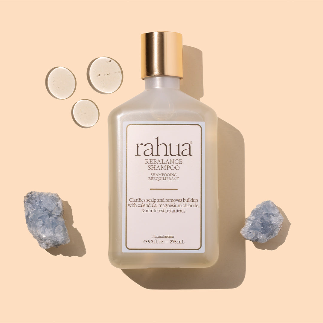 Rahua | Rebalance Shampoo | Styled Image with Swatch_Oct26 - shampoo bottle with gold cap, crystals and swatch against a beige background