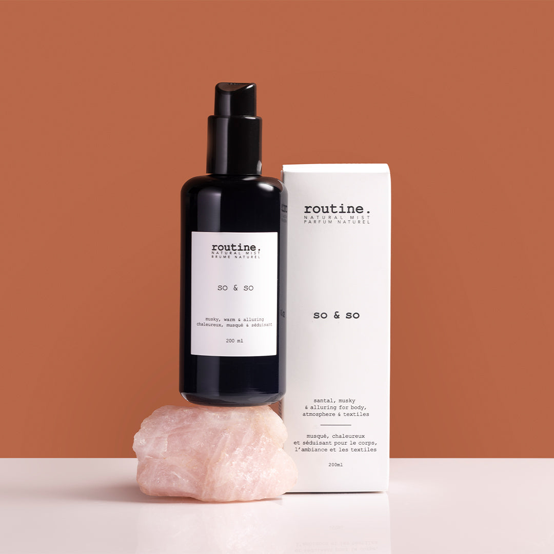 Routine | Body, Hair & Atmosphere Mist - So & So | Styled Image with Swatch_Aug26 - black bottle with a white box, displayed on a rose quartz stone against a warm earth tone background