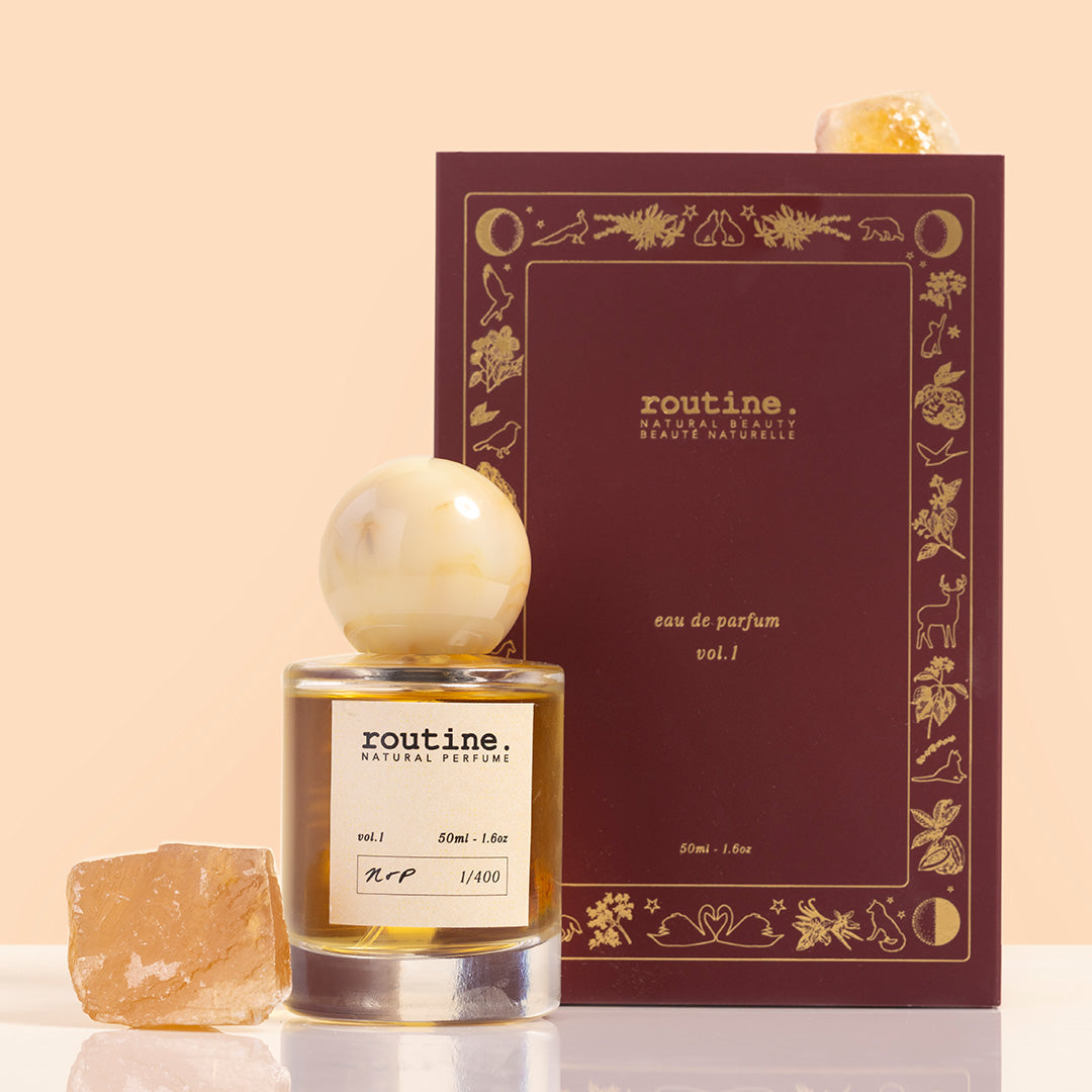 Routine | Natural Perfume Volume 1 | Styled image of glass perfume bottle with beige label with white cap and blue book looking box 