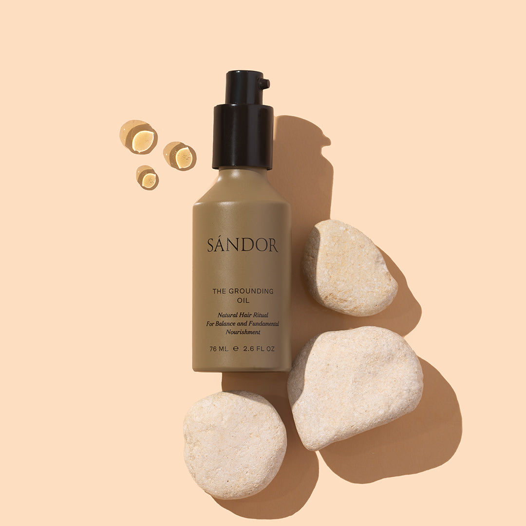 Sándor | The Grounding Oil | Styled Image - oil bottle styled with oil droplets and white stones on a beige background