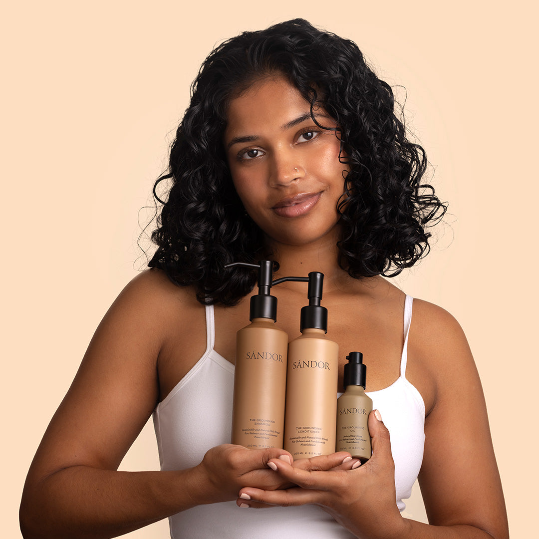 Sándor Discovery | Model holding products | Model holding three brown bottles with black pumps standing against a beige background