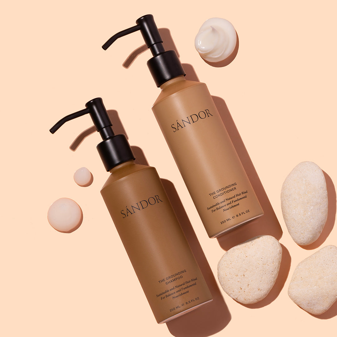 Sándor | The Grounding Shampoo and Conditioner | Flat lay with swatches | Two brown bottles with black pumps on peach background with white product swatches 