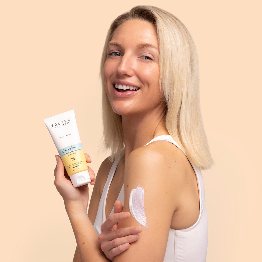 Solara Suncare | Clean Freak SPF 30 | Model Image with Swatch - person holding tube on peach background with white product swatch on arm
