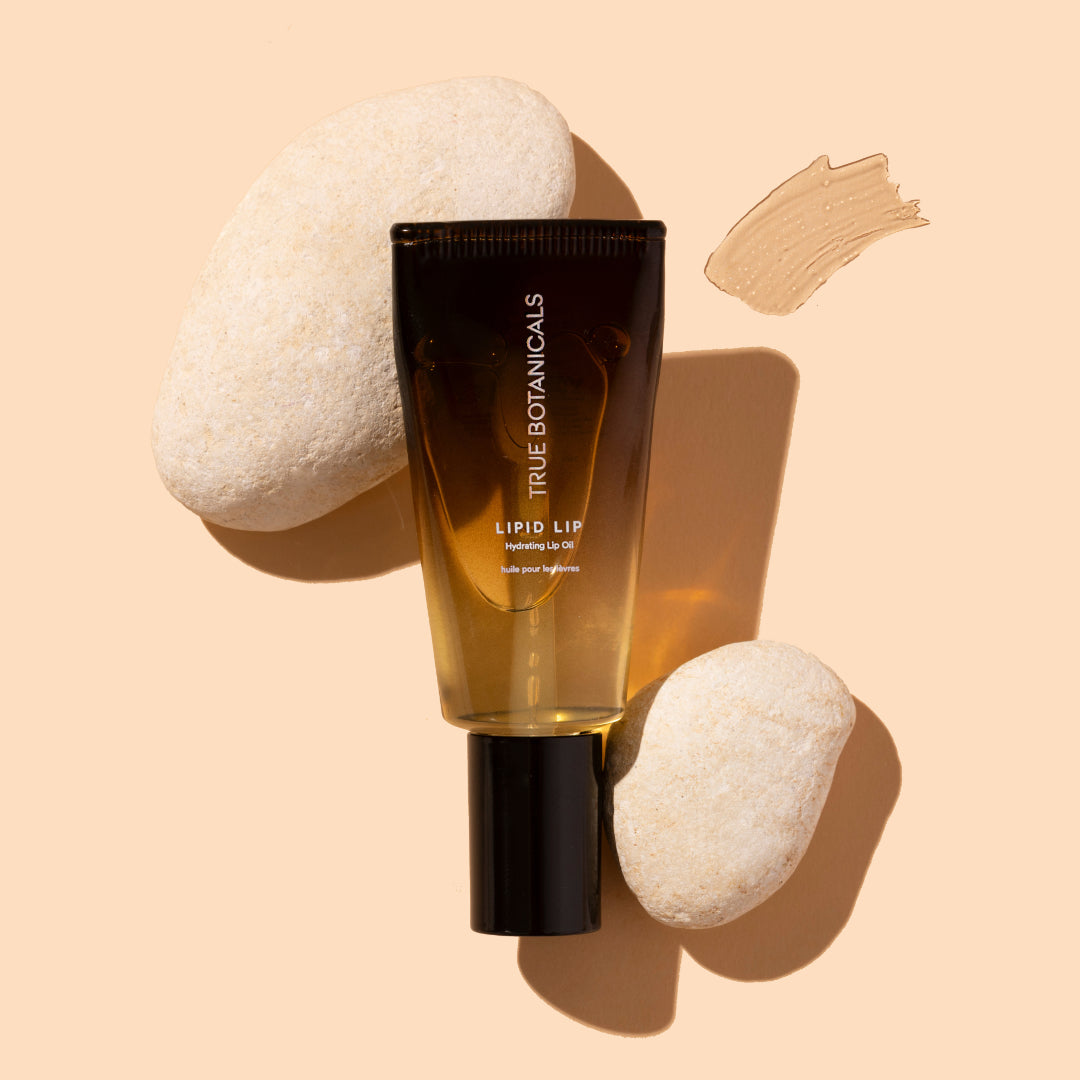 True Botanicals | Lipid Lip Hydrating Lip Oil | Product Image with Swatch - oil tube with stones on a warm background