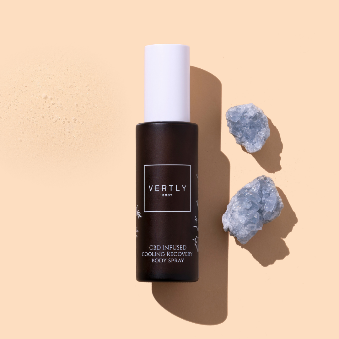 Vertly | Cooling Recovery Body Spray | Styled Image - dark amber bottle with a white cap, displayed on a beige background alongside crystals and a fine mist texture