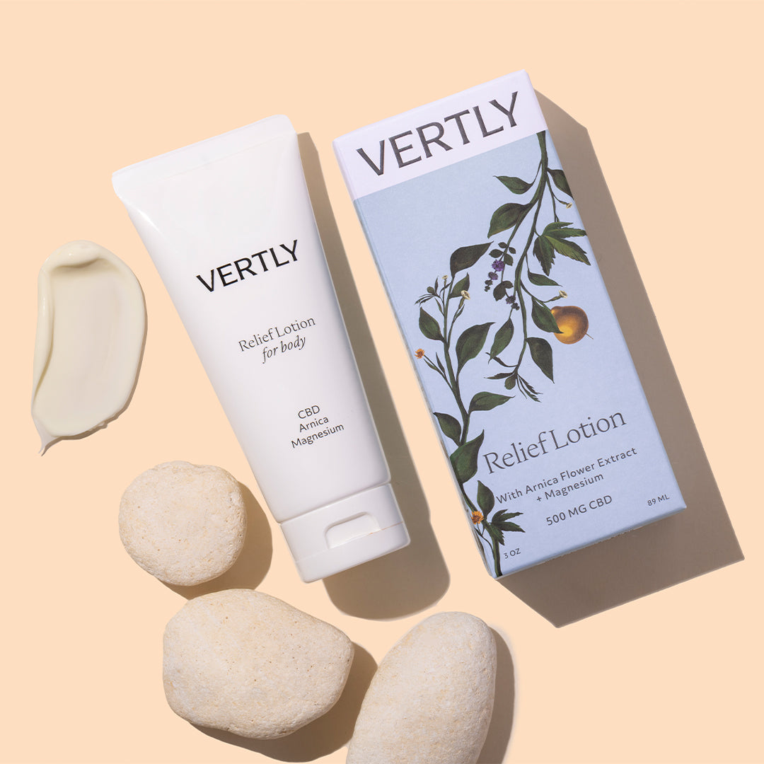 Vertly | Relief Lotion | Styled Image with Swatch_Jul26 - white tube with matching box, lotion swatch, and white stones on a beige background