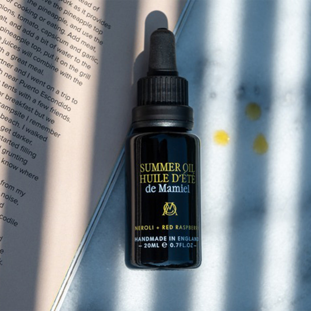 de Mamiel | Summer Facial Oil | Lifestyle Book Shot - Oil bottle placed beside an open book in natural sunlight
