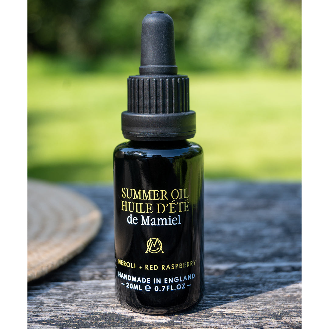 de Mamiel | Summer Facial Oil | Outdoor Product Shot - oil bottle standing outdoors on a wooden surface